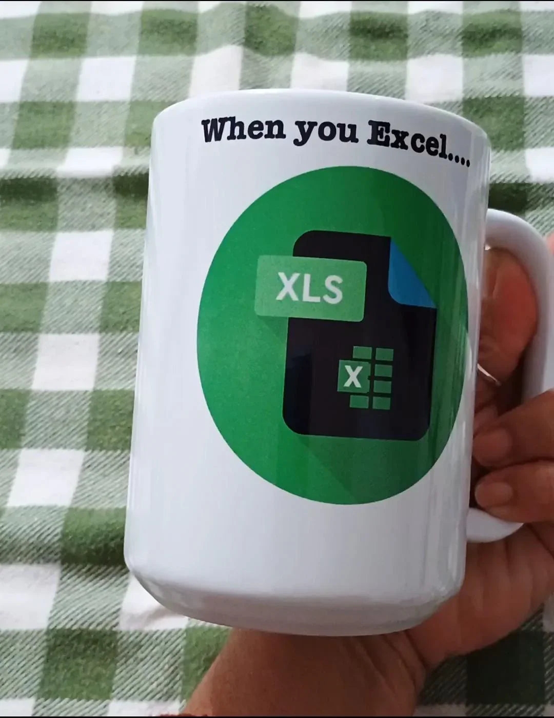 White mug with Excel XLS file icon and text 'When you Excel...' on green checkered tablecloth