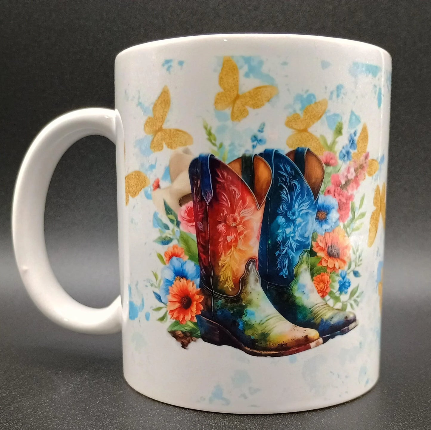 White ceramic mug with colorful cowboy boots, orange and blue flowers, and gold butterflies design