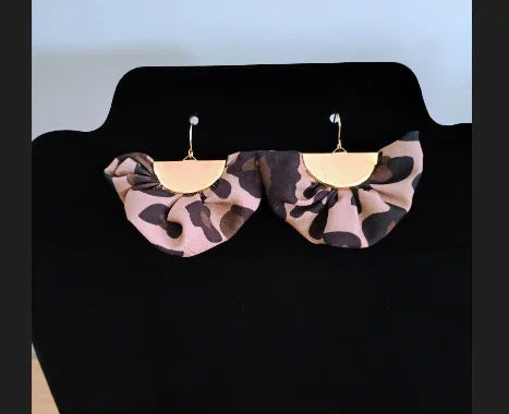 Gold half-circle earrings with ruffled leopard print fabric on black display stand