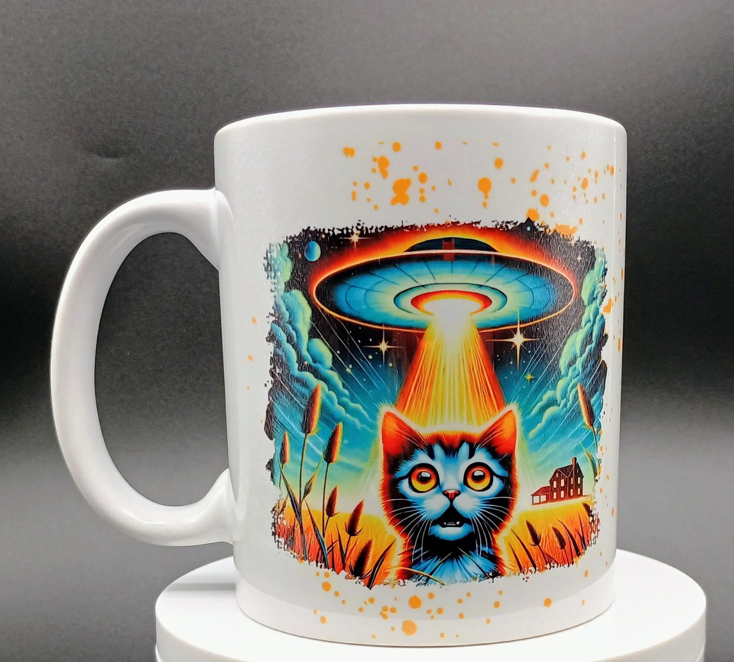 White mug with vibrant illustration of a wide-eyed cat under a glowing UFO beam in a field