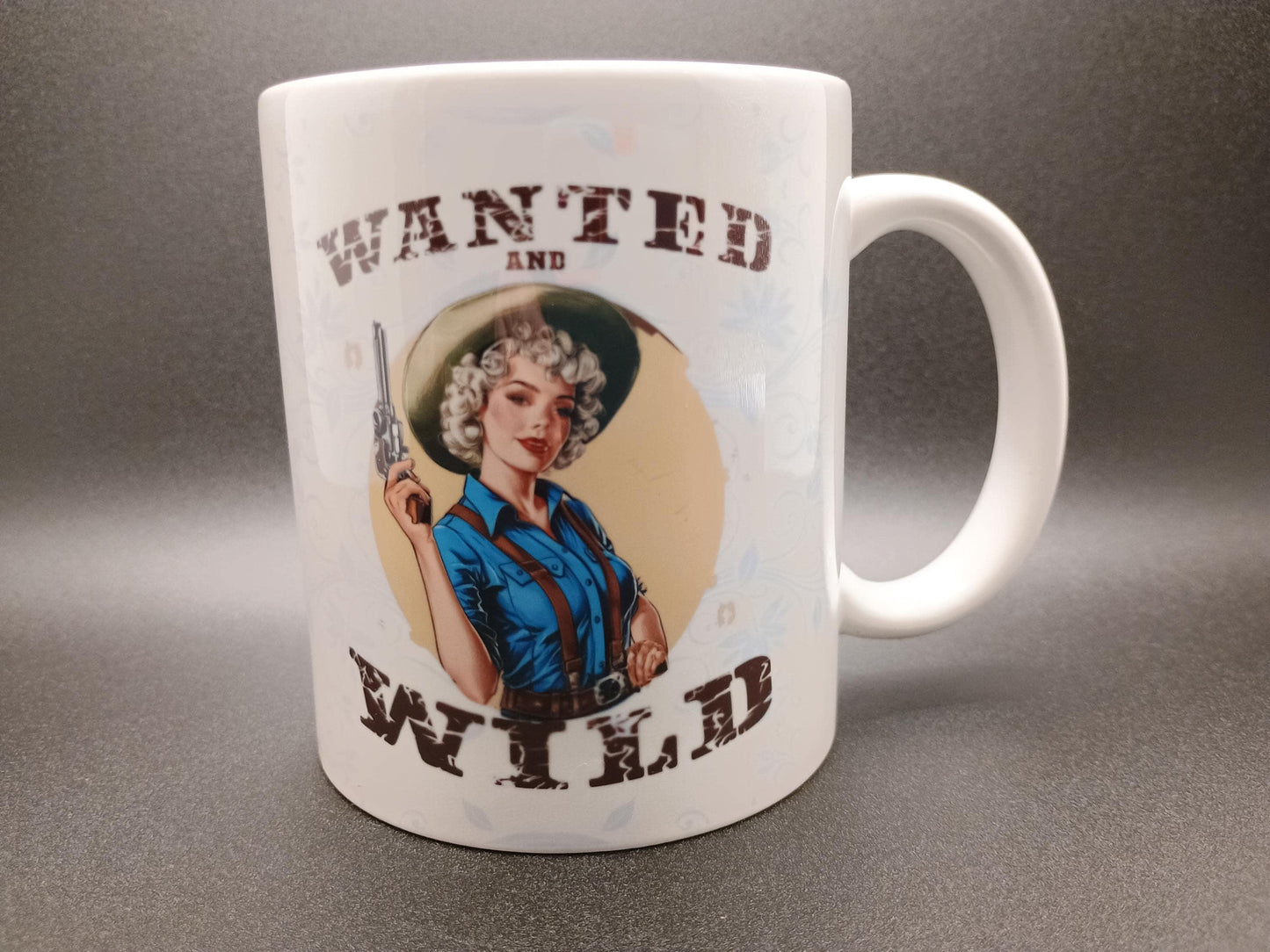 White mug with vintage pin-up cowgirl holding a revolver and text Wanted and Wild