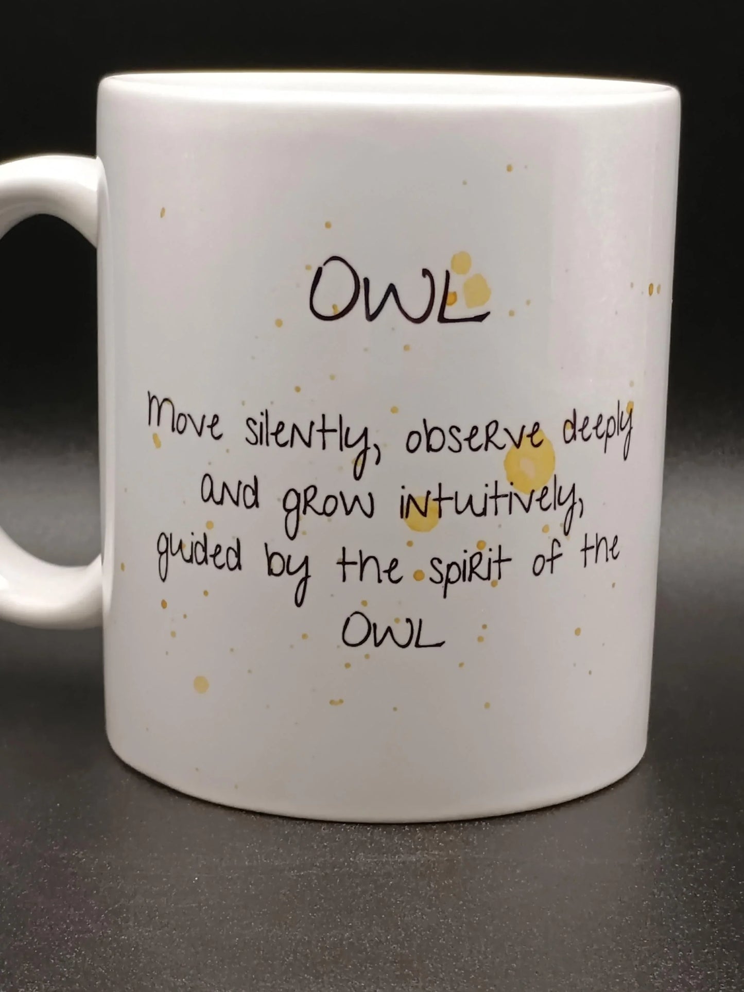 White ceramic mug with inspiring owl quote and scattered brown spots on black background