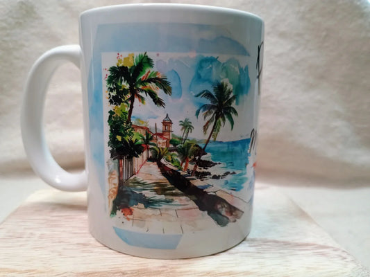 White ceramic mug with watercolor print of palm trees, ocean, and coastal walkway under blue sky