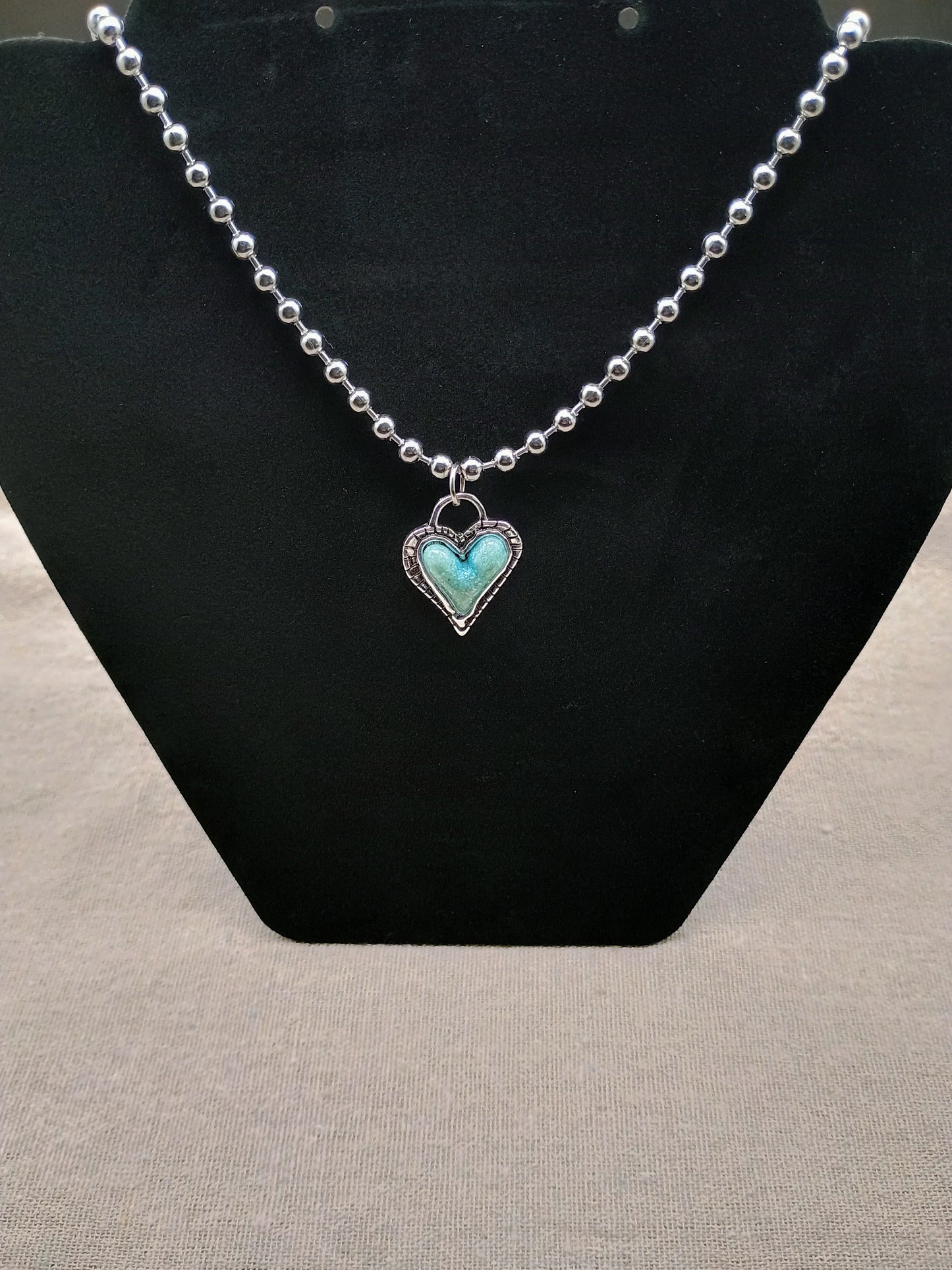 Silver ball chain necklace with turquoise heart pendant on black display stand