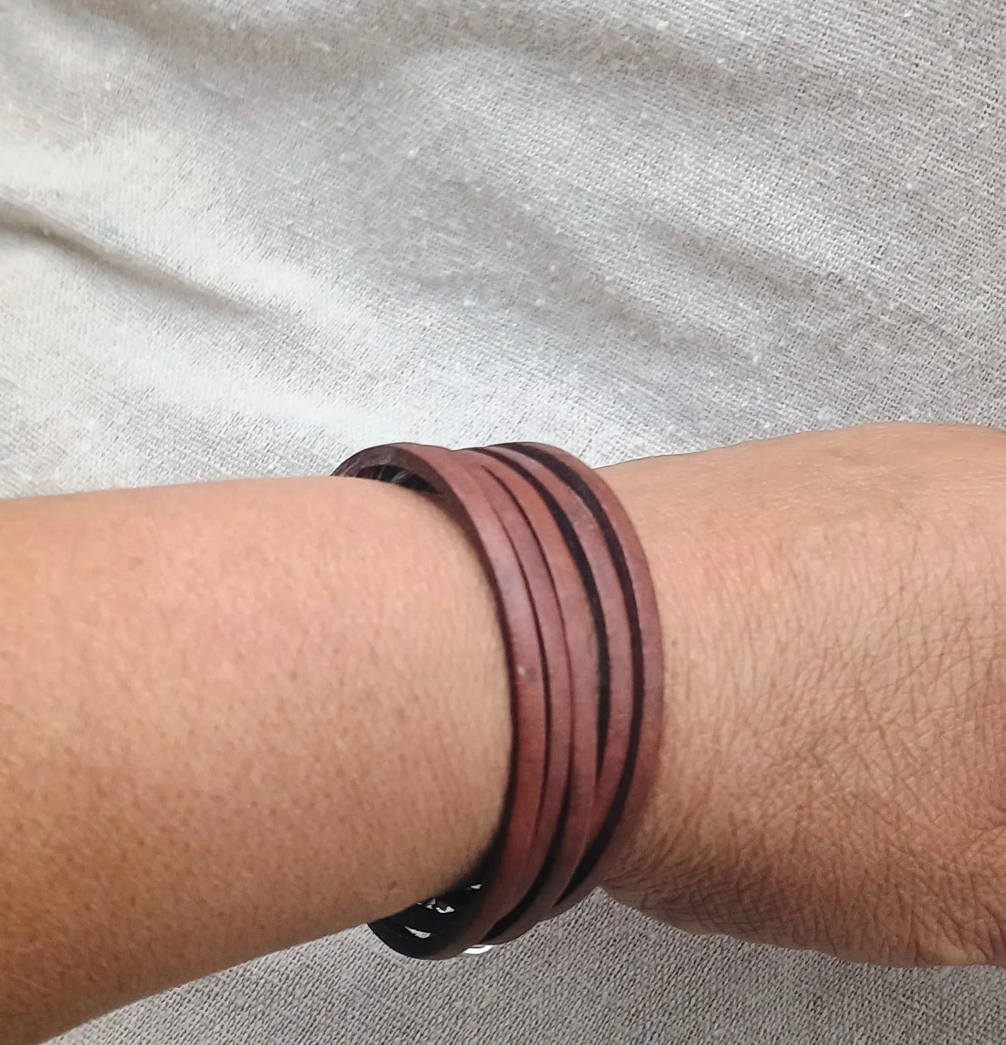 Wrist wearing a brown multi-strand leather bracelet on a light fabric background