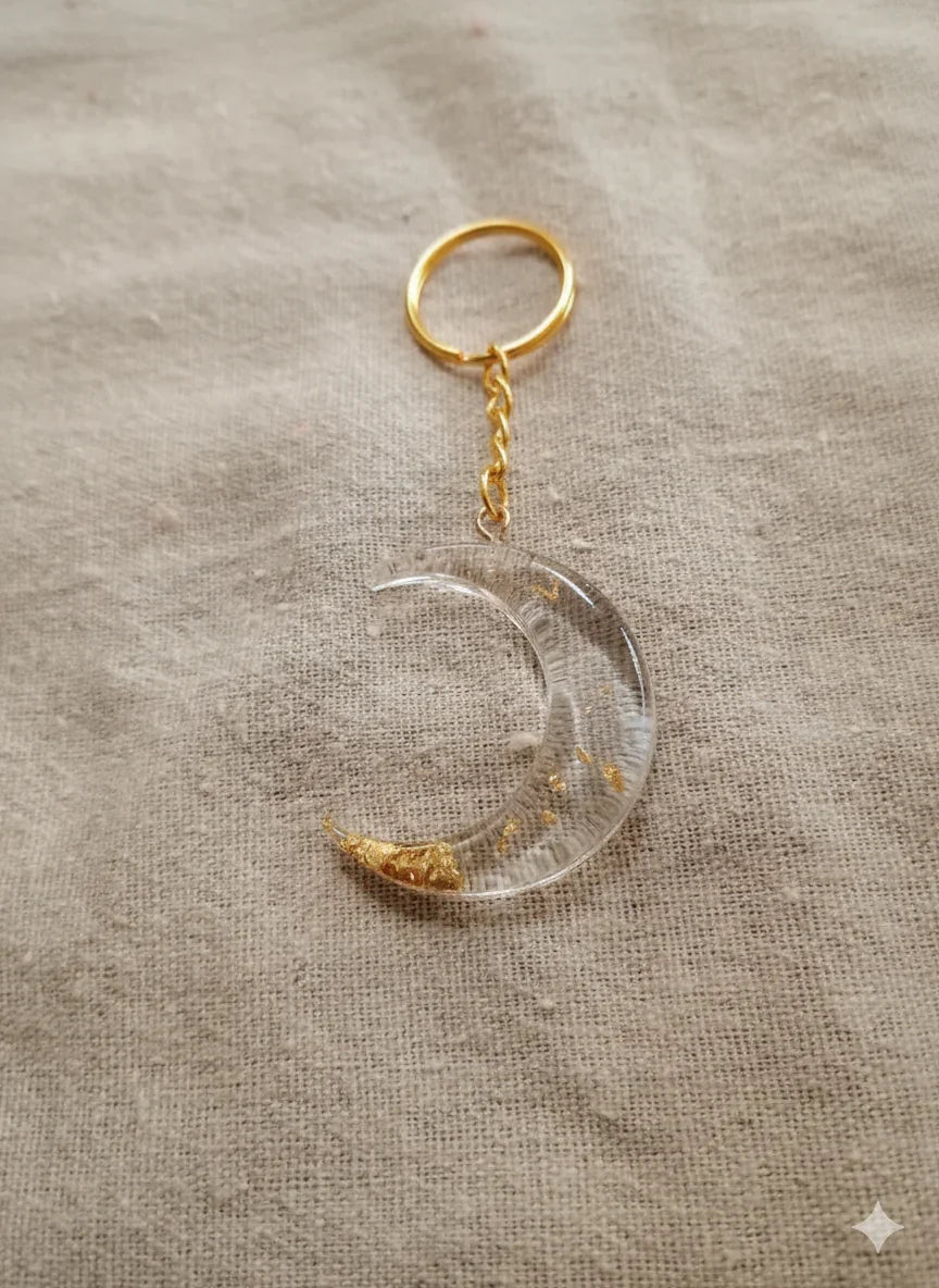 Transparent crescent moon keychain with gold flakes on beige fabric background