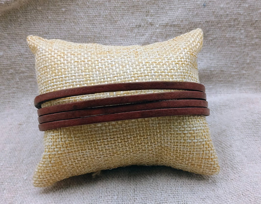 Brown leather bracelet displayed on a beige woven fabric cushion with textured background