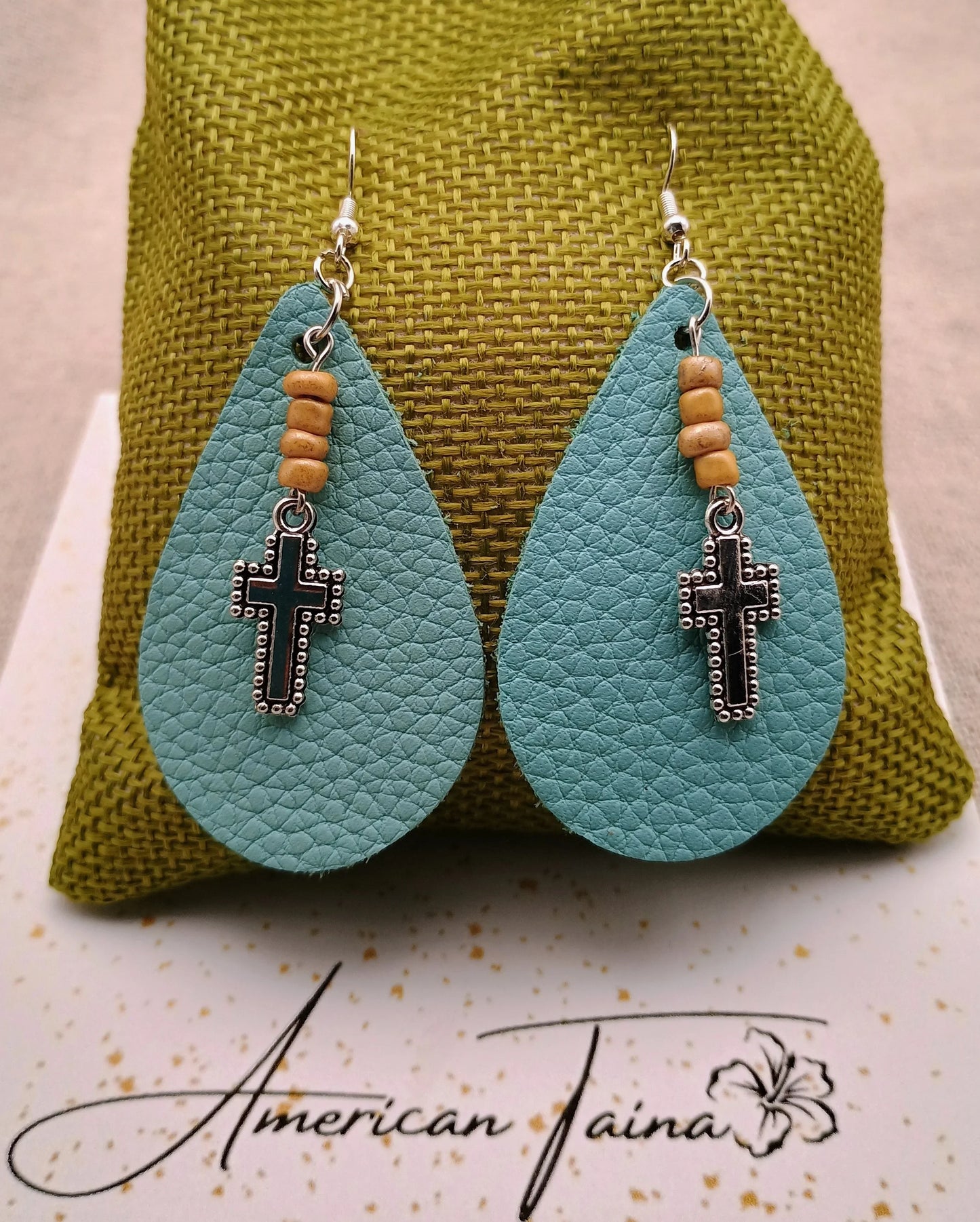 Teardrop turquoise leather earrings with wooden beads and black cross charms on olive green fabric