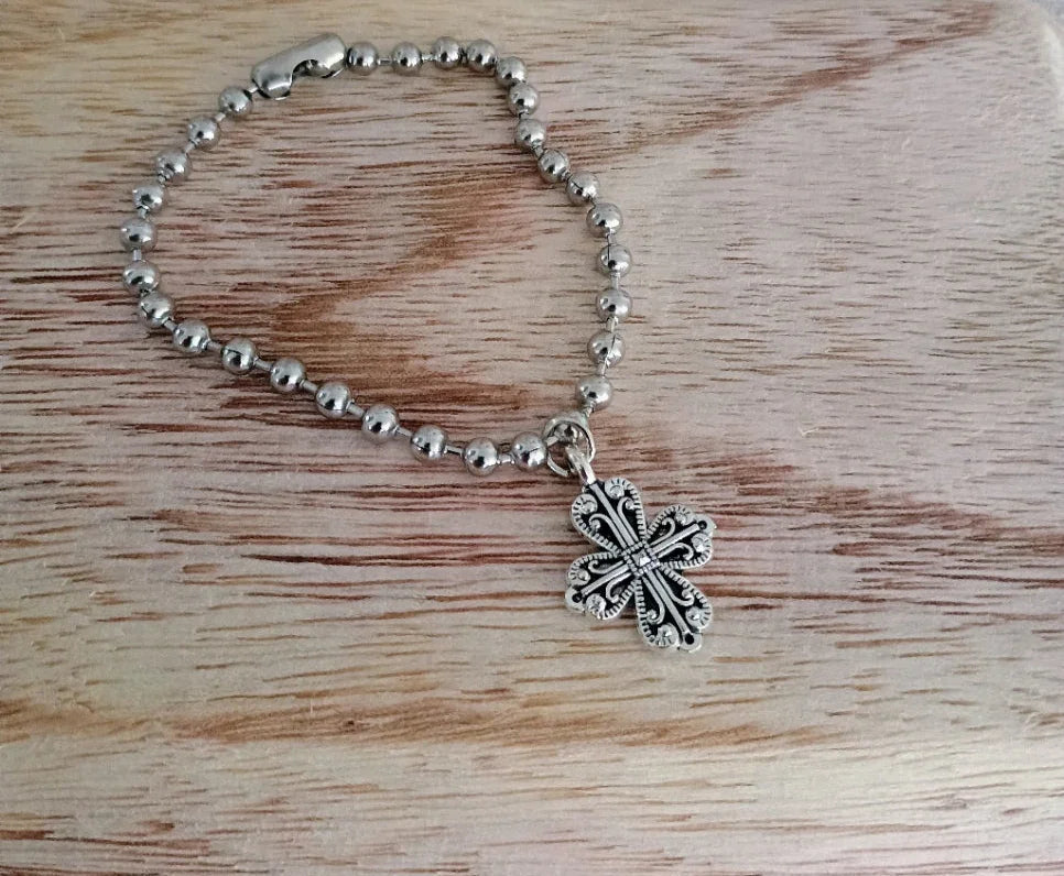 Silver beaded bracelet with a detailed ornamental cross charm on wooden surface