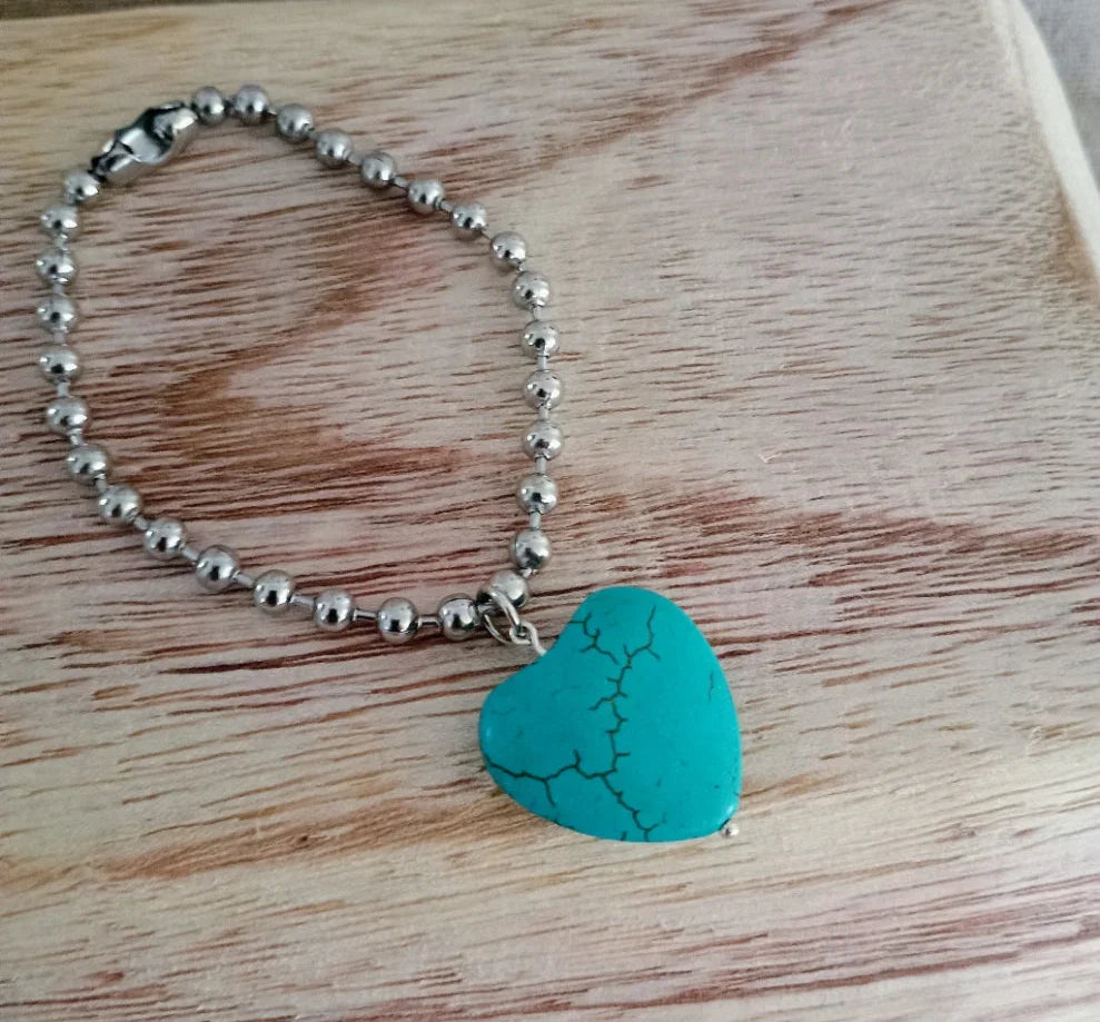 Silver beaded bracelet with a turquoise heart-shaped pendant on wooden surface
