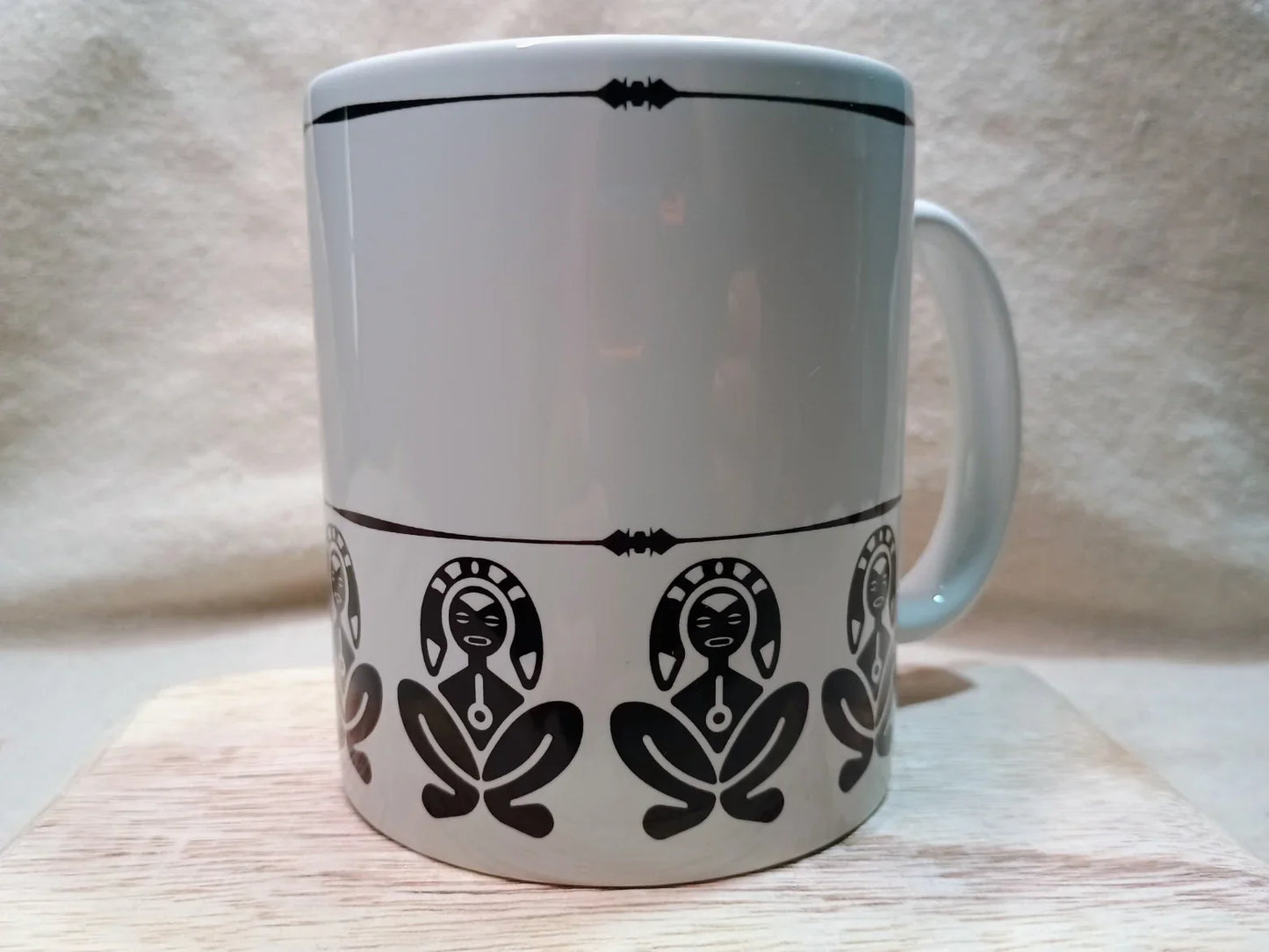 White ceramic mug with black Taino indigenous figure designs and decorative border
