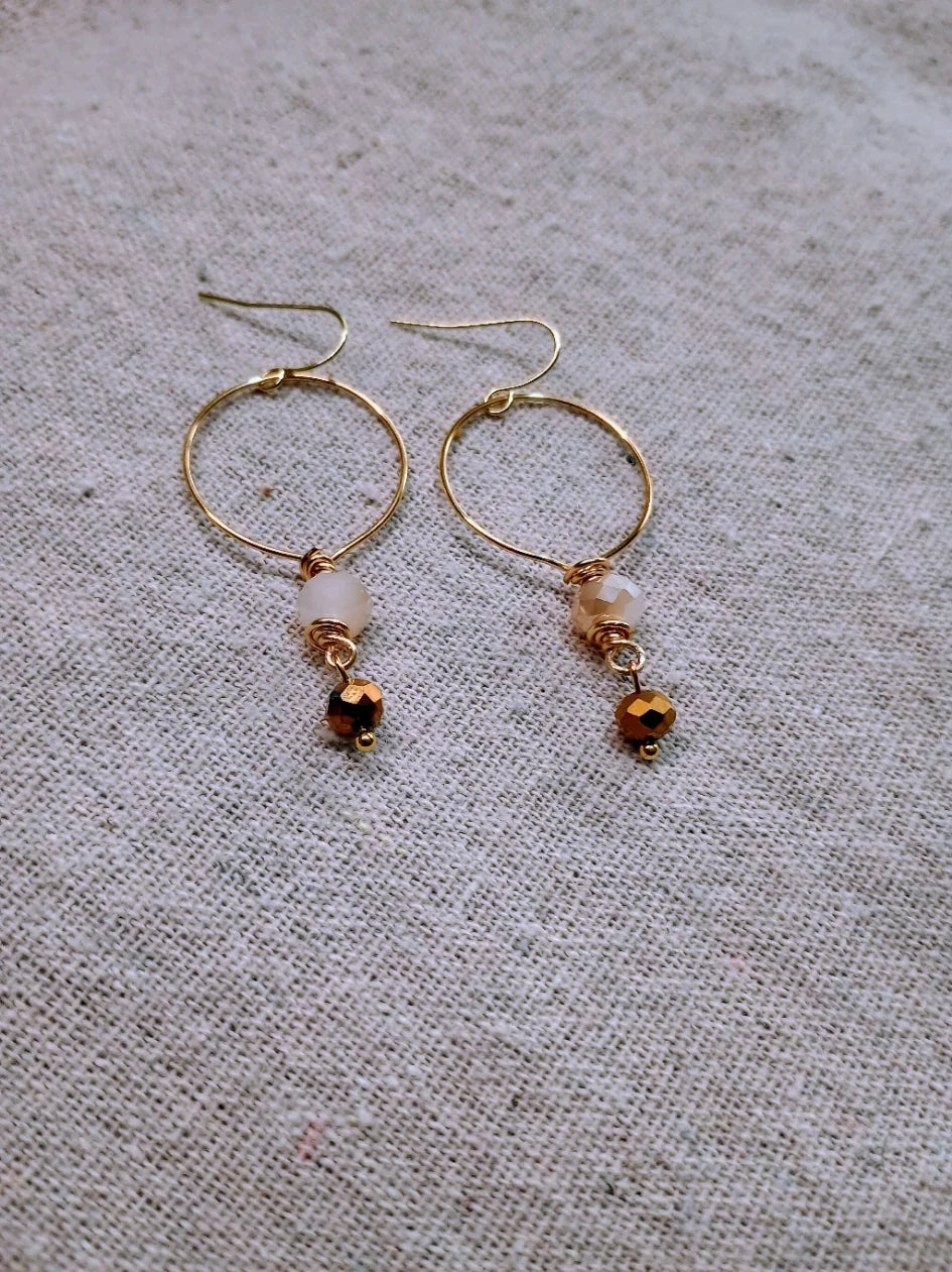 Delicate gold-tone hoop earrings with small faceted beads on beige fabric background