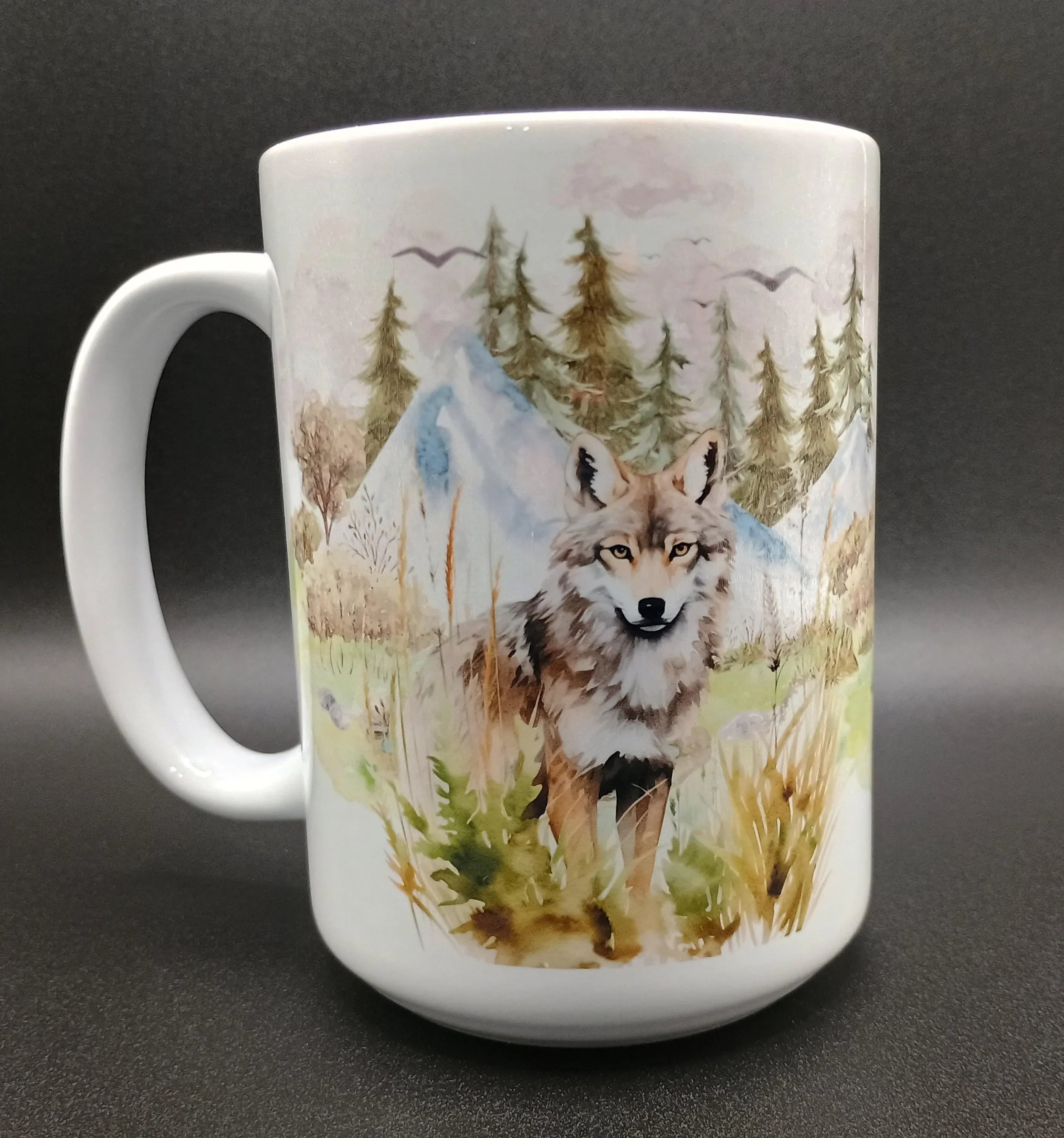 White ceramic mug with watercolor-style wolf and forest landscape design featuring trees, mountains, and birds