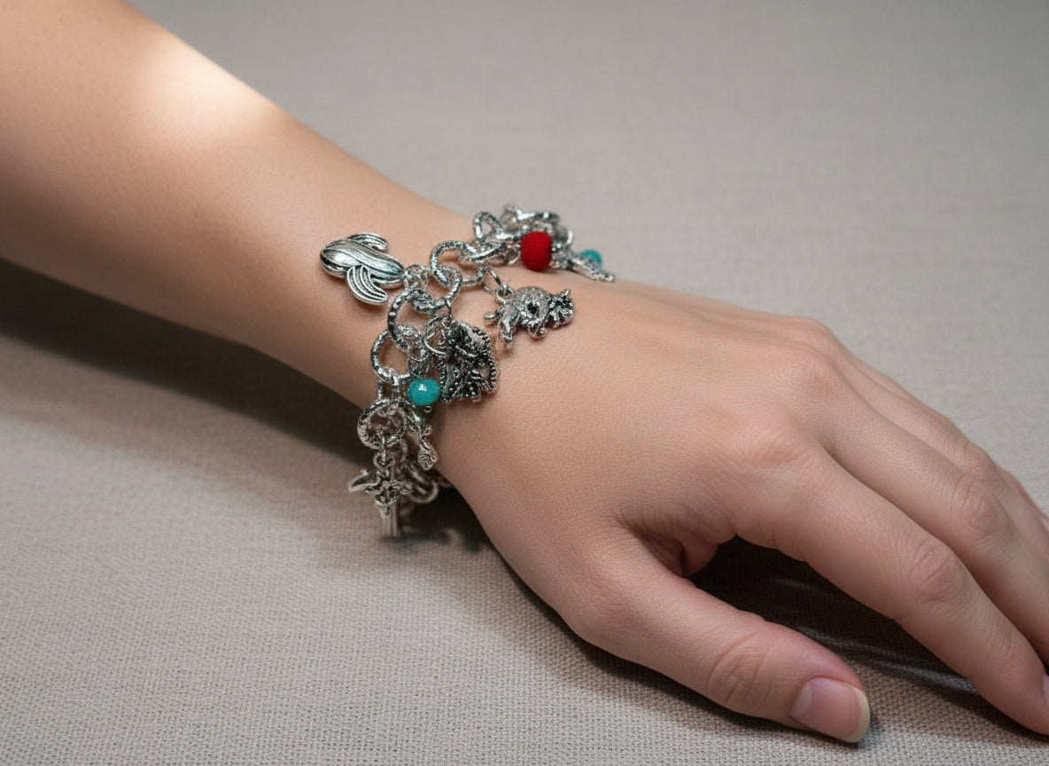 Hand wearing silver charm bracelet with various detailed charms and colored beads on gray fabric