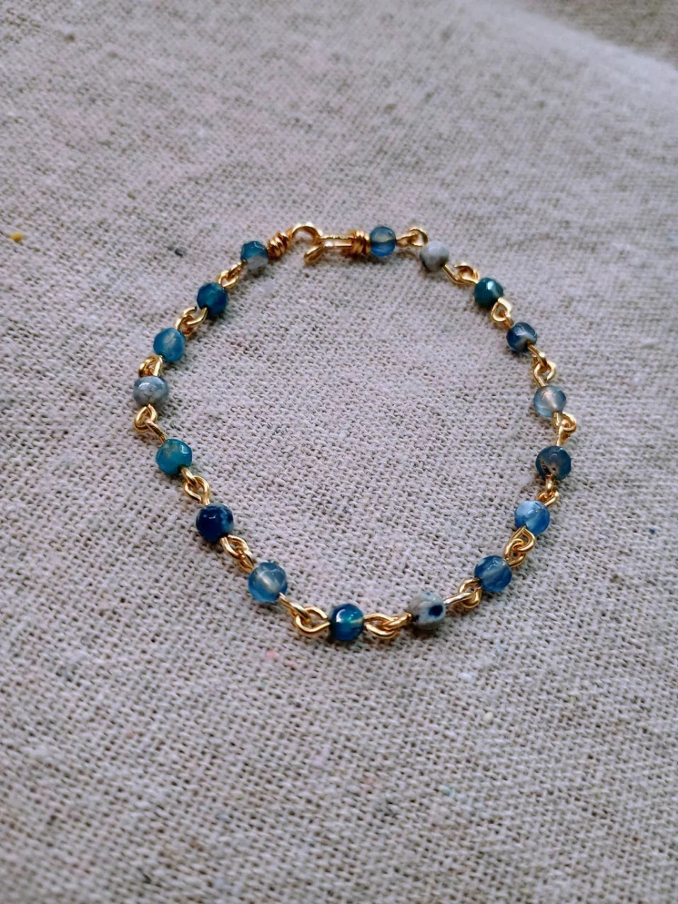 Blue agate bead bracelet with gold links on light beige fabric background