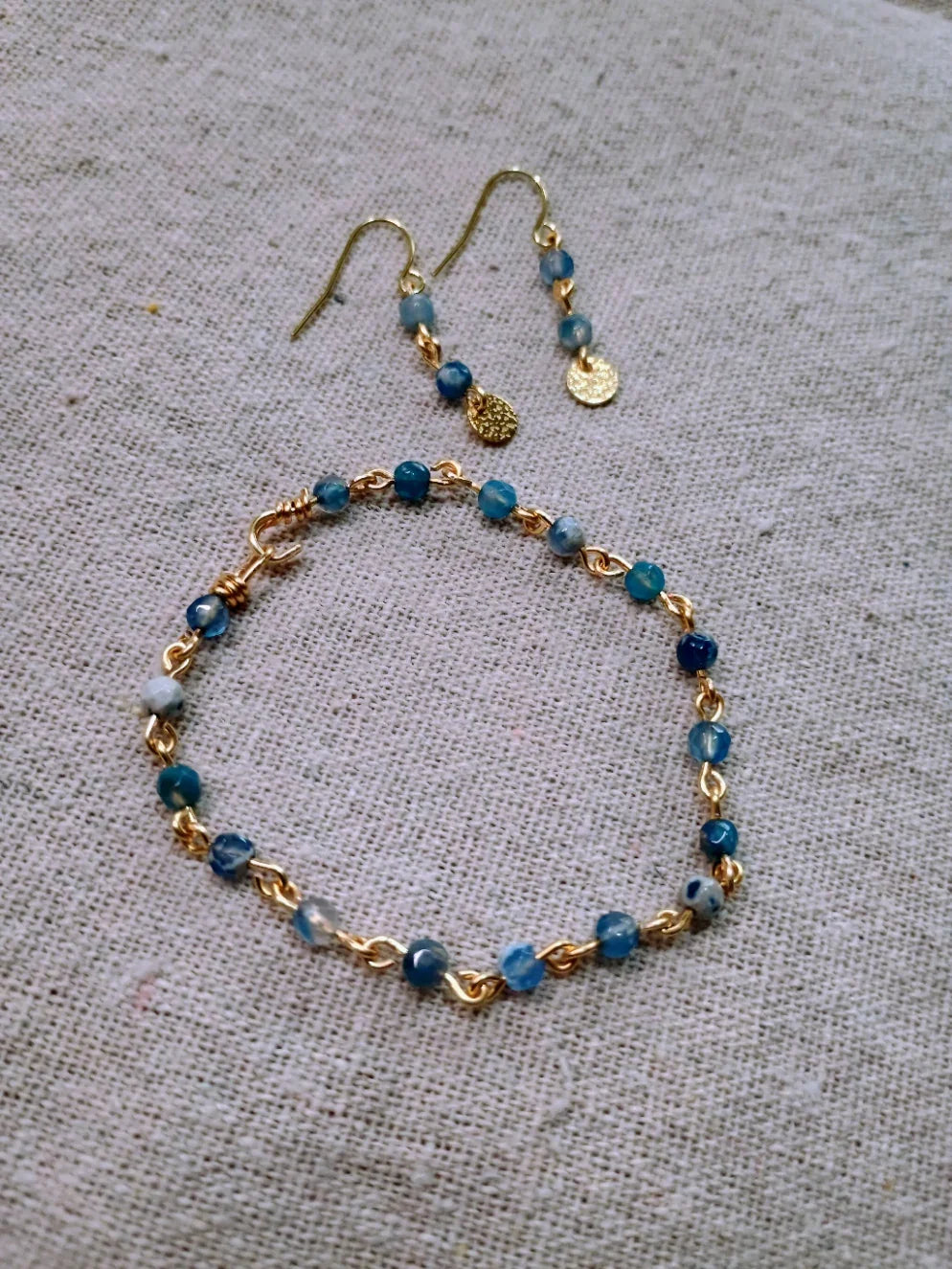 Blue agate beaded bracelet and matching gold drop earrings on beige fabric background