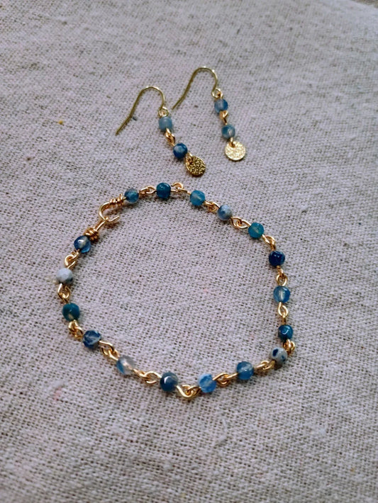 Blue agate beaded bracelet and matching gold drop earrings on beige fabric background