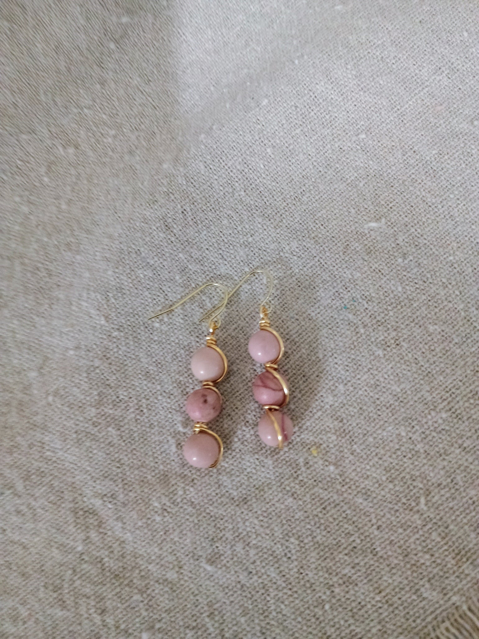 Pink beaded dangle earrings with gold wire wrap on beige fabric background