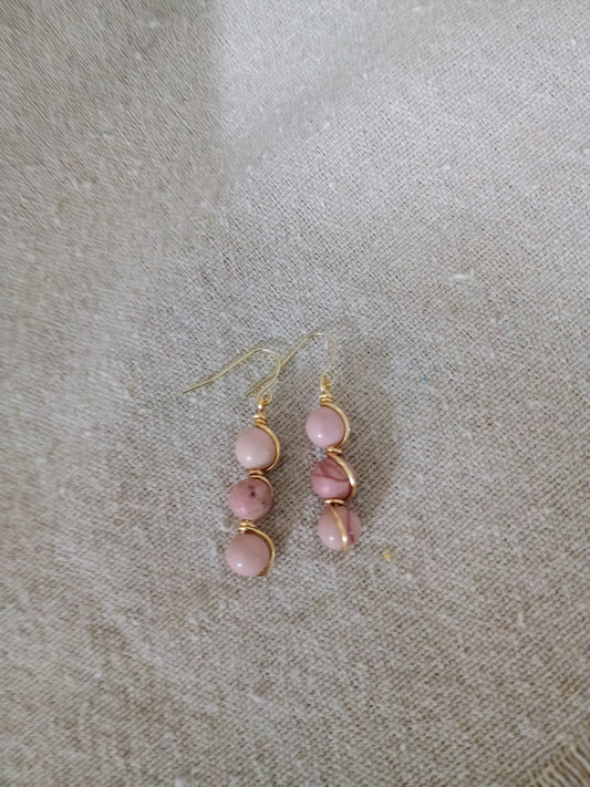 Pink beaded dangle earrings with gold wire wrap on beige fabric background