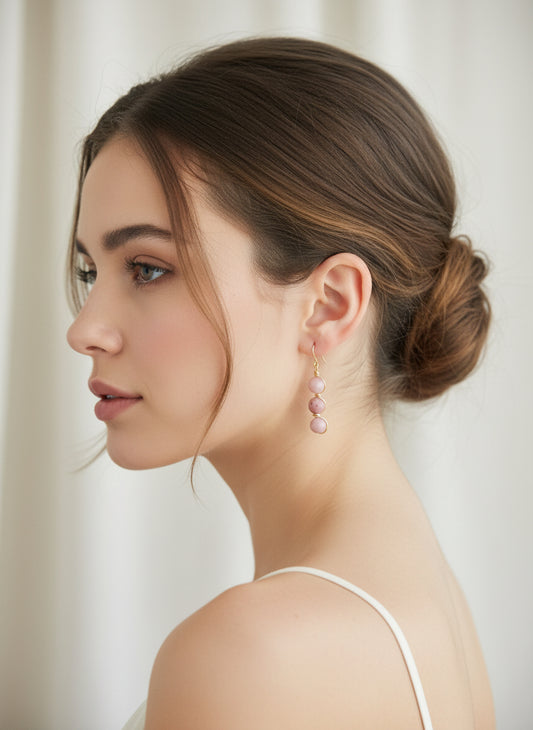 Profile of woman with blush pink gemstone drop earrings and brown hair in a low bun