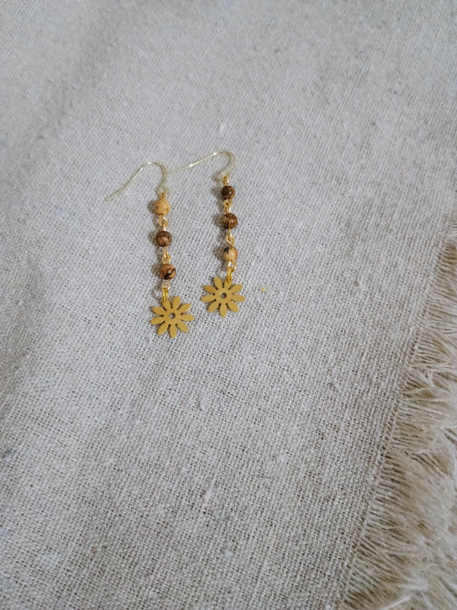 Pair of dangle earrings with brown natural stone beads and gold sun-shaped charms on beige fabric