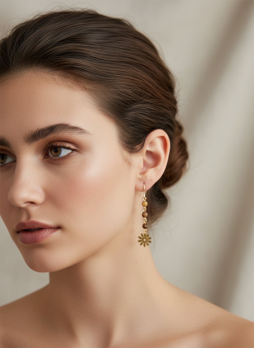 Close-up of woman wearing brown natural stone dangle earrings with gold flower charm