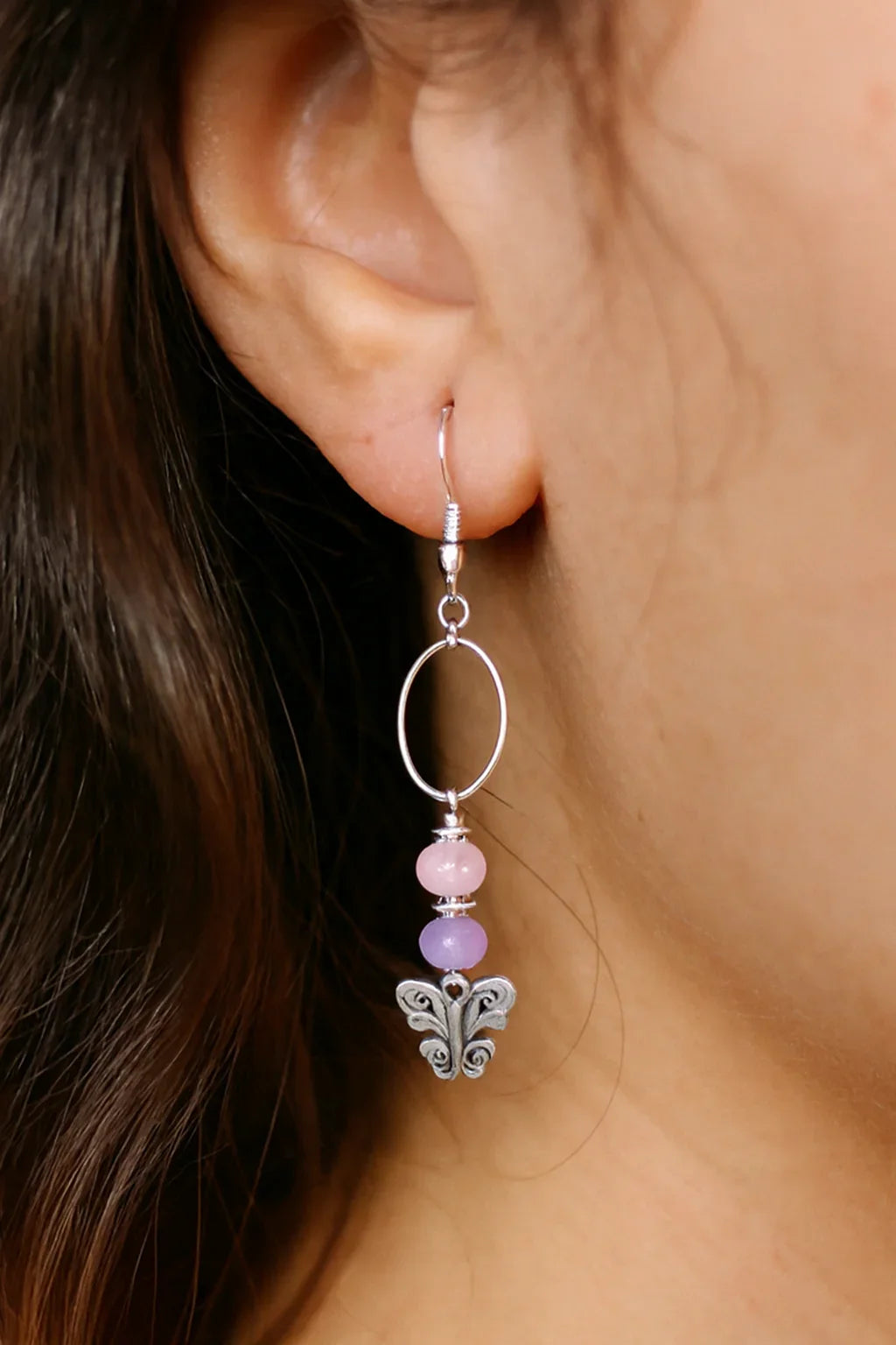 Close-up of a silver dangle earring with pink and purple beads and butterfly charm on ear