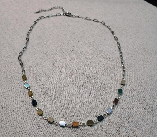 Silver chain hematite necklace with multicolored hexagonal beads on beige fabric background