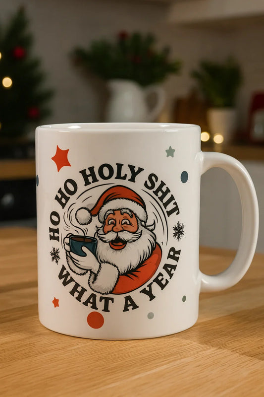White Christmas mug with Santa holding coffee and text 'Ho Ho Holy Shit What A Year' on wooden table