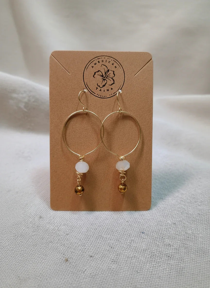 Gold tone hoop earrings with white and brown beads on a branded card