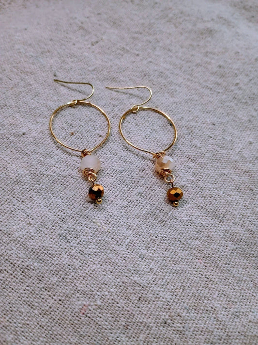 Delicate gold-tone hoop earrings with small faceted beads on beige fabric background